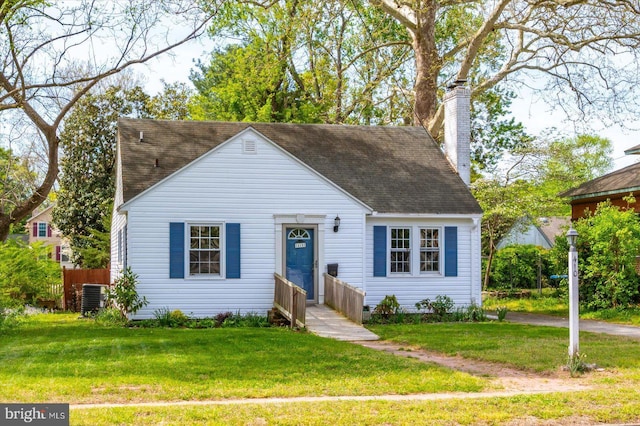 view of front of property with central AC, a chimney, a front yard, and roof with shingles
