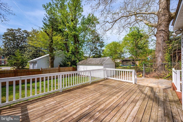 deck featuring a fenced backyard, a storage unit, an outbuilding, a detached garage, and a lawn