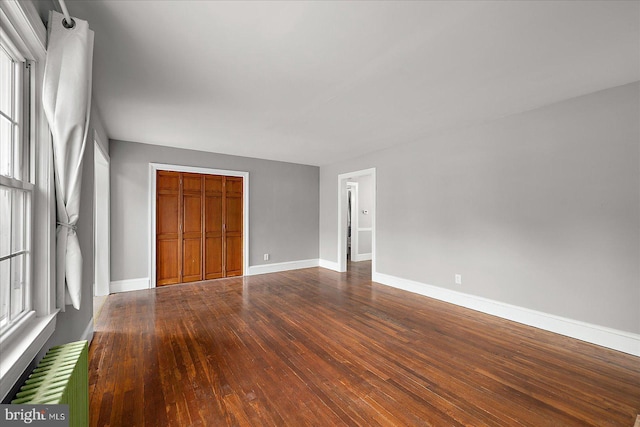 unfurnished bedroom featuring wood-type flooring, radiator, a closet, and baseboards