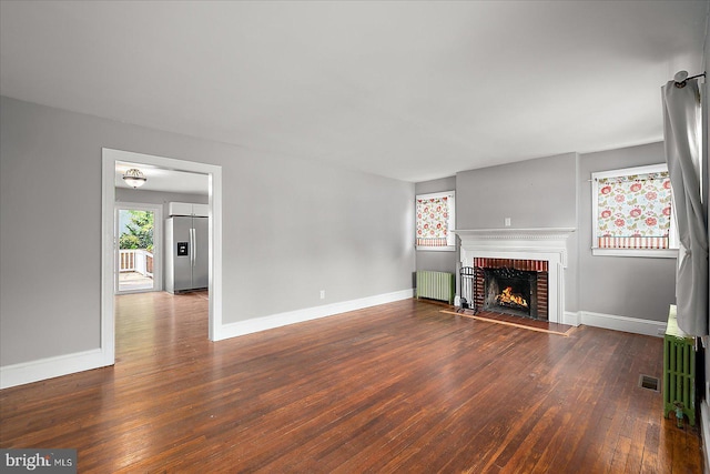 unfurnished living room with a fireplace, visible vents, radiator heating unit, baseboards, and hardwood / wood-style floors