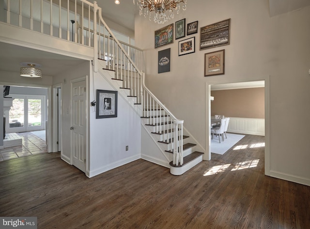 staircase with a towering ceiling, wood finished floors, a notable chandelier, and baseboards