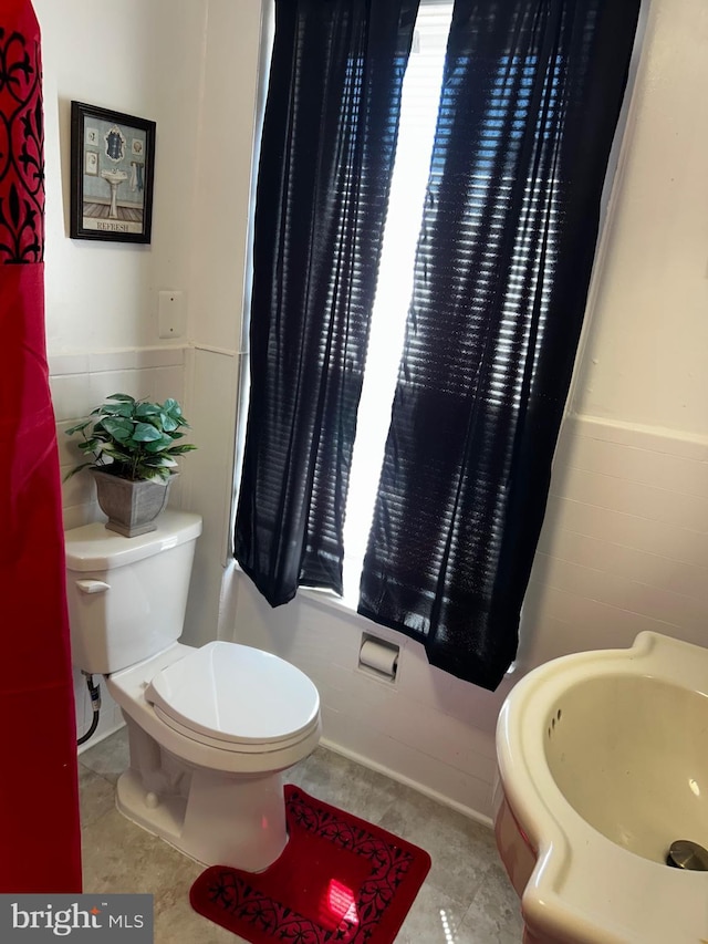 bathroom with tile patterned floors, toilet, wainscoting, and tile walls