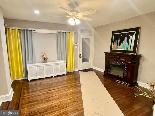 living room featuring radiator heating unit, a ceiling fan, wood finished floors, and baseboards
