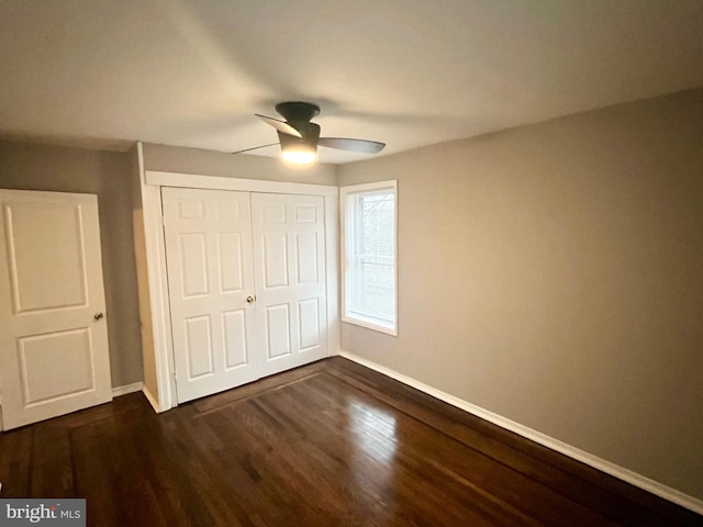 unfurnished bedroom with dark wood-style floors, a closet, baseboards, and a ceiling fan