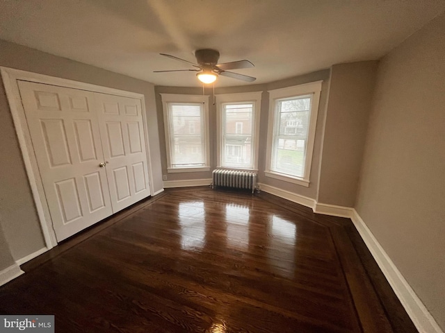 unfurnished bedroom featuring ceiling fan, dark wood-type flooring, a closet, radiator heating unit, and baseboards