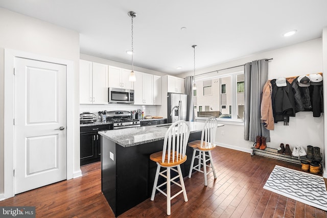 kitchen featuring dark wood-type flooring, a center island with sink, stainless steel appliances, a breakfast bar area, and decorative backsplash