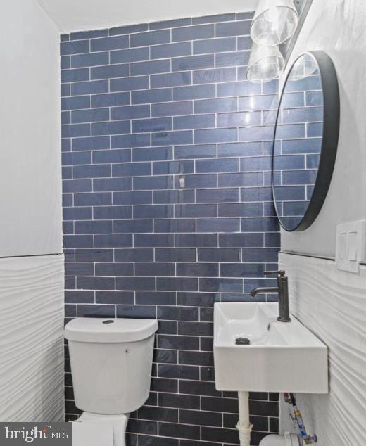 half bath with a sink, tile walls, and toilet