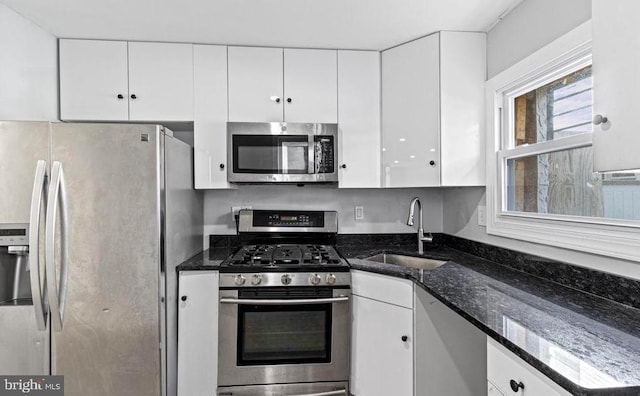 kitchen featuring dark stone countertops, white cabinets, appliances with stainless steel finishes, and a sink