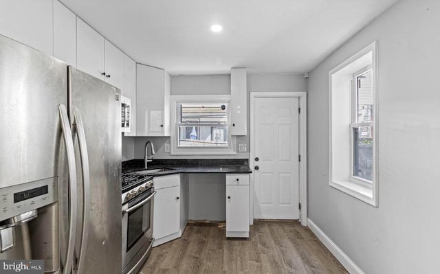 kitchen featuring wood finished floors, a sink, dark countertops, stainless steel appliances, and white cabinetry