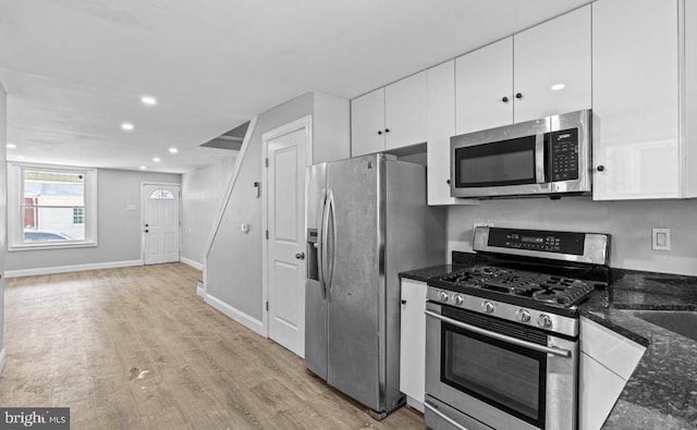 kitchen featuring stainless steel appliances, dark stone counters, light wood-style flooring, white cabinetry, and baseboards
