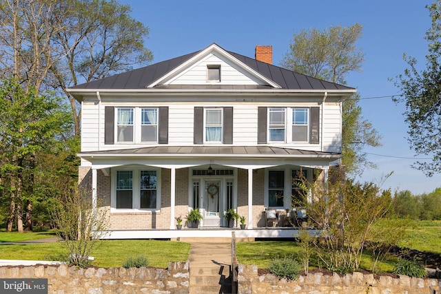 view of front of home with a chimney, a standing seam roof, brick siding, metal roof, and a porch