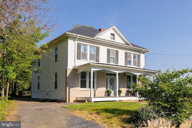 view of front facade with covered porch, a chimney, a standing seam roof, brick siding, and metal roof