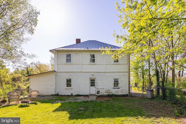 back of property with a fire pit, a chimney, a standing seam roof, metal roof, and a lawn