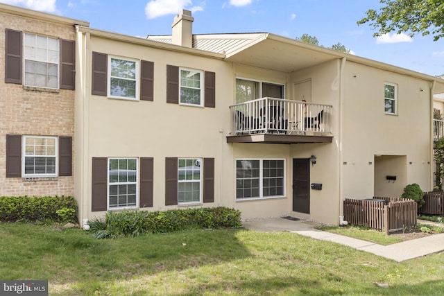 back of property with a balcony, stucco siding, and a chimney