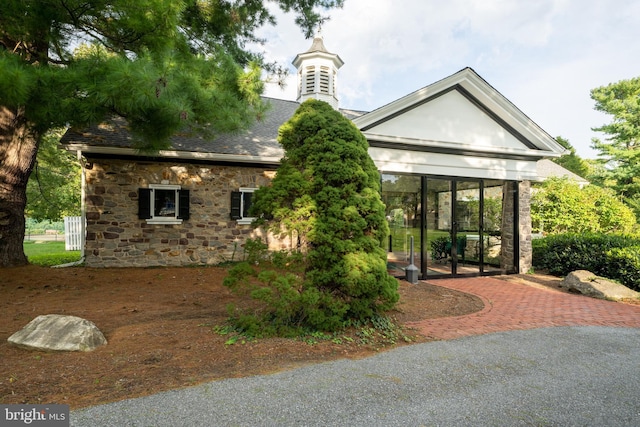 rear view of property featuring stone siding, a sunroom, and roof with shingles