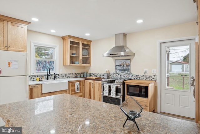 kitchen with light brown cabinets, range with two ovens, freestanding refrigerator, black microwave, and wall chimney exhaust hood