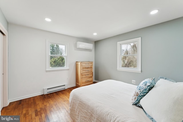 bedroom with baseboard heating, multiple windows, an AC wall unit, and hardwood / wood-style flooring