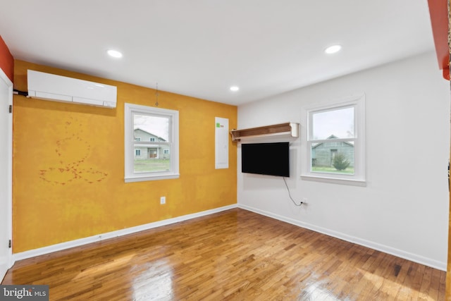 unfurnished living room with a wall mounted air conditioner, baseboards, plenty of natural light, and wood finished floors
