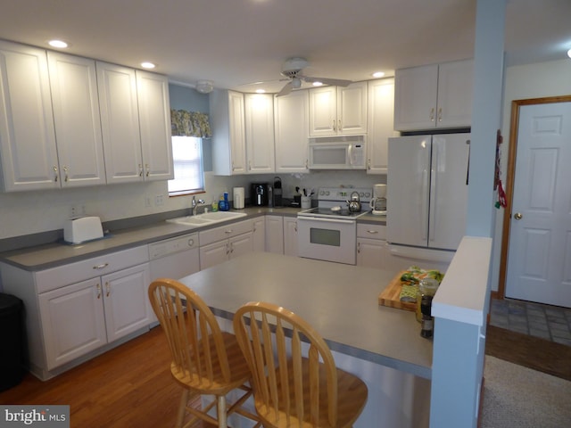 kitchen featuring a ceiling fan, a kitchen bar, a sink, white cabinetry, and white appliances