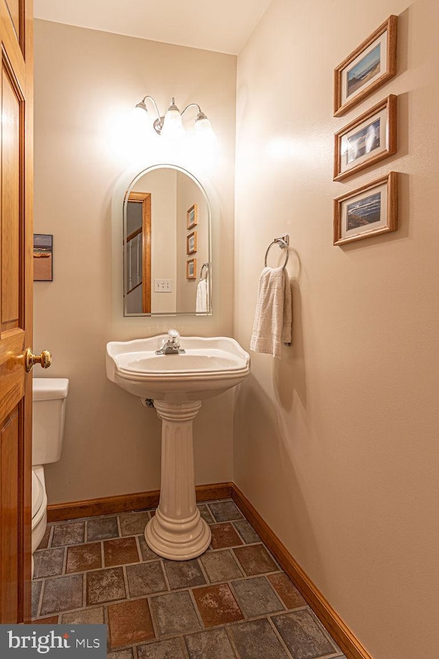 bathroom featuring toilet, baseboards, and stone tile flooring