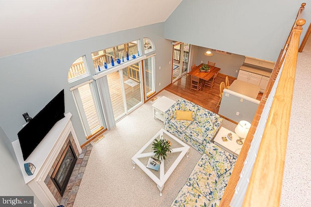 living area featuring a glass covered fireplace, high vaulted ceiling, and carpet