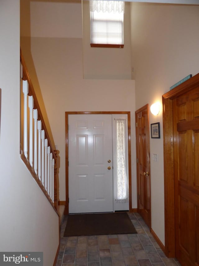 foyer entrance featuring stairway, baseboards, a towering ceiling, and stone finish flooring