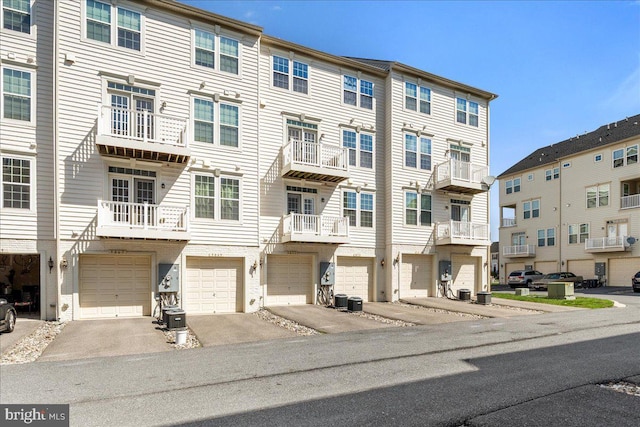 view of building exterior with driveway, an attached garage, central AC, and a residential view