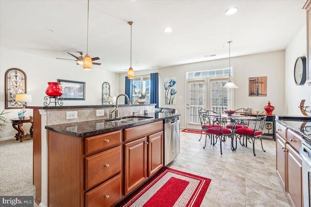 kitchen with dishwasher, dark stone counters, a sink, hanging light fixtures, and brown cabinetry