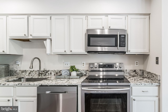 kitchen featuring light stone counters, stainless steel appliances, white cabinets, and a sink