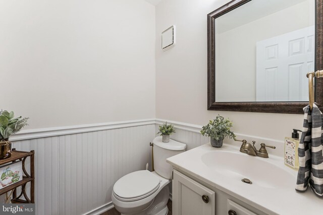 half bath featuring toilet, vanity, and wainscoting