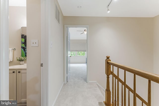 corridor featuring rail lighting, light carpet, an upstairs landing, baseboards, and visible vents