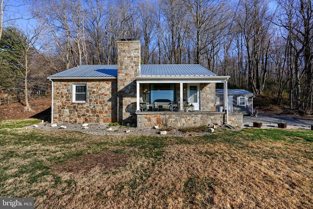 view of front facade featuring a front yard, stone siding, metal roof, a chimney, and a standing seam roof