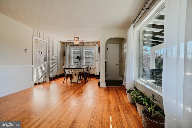 dining room featuring light wood-type flooring, arched walkways, wainscoting, and a ceiling fan