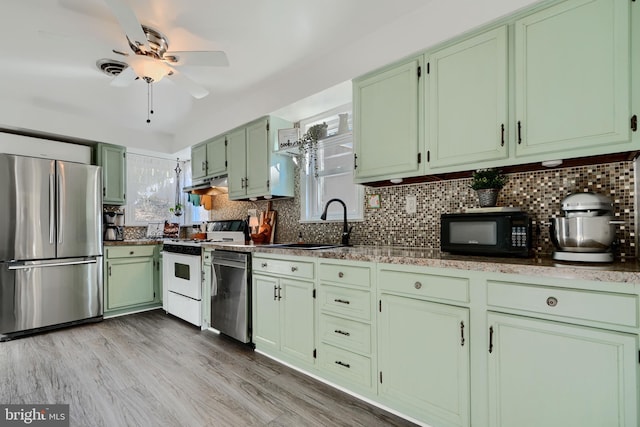 kitchen featuring green cabinetry, a sink, appliances with stainless steel finishes, under cabinet range hood, and backsplash