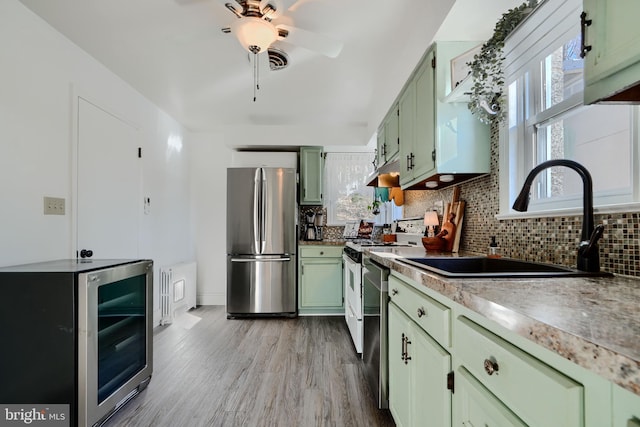 kitchen with a sink, freestanding refrigerator, green cabinets, backsplash, and beverage cooler