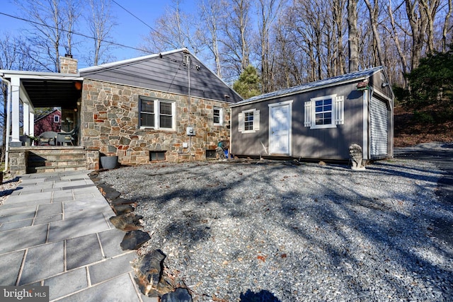 view of front of home with an outdoor structure, a chimney, stone siding, a porch, and metal roof