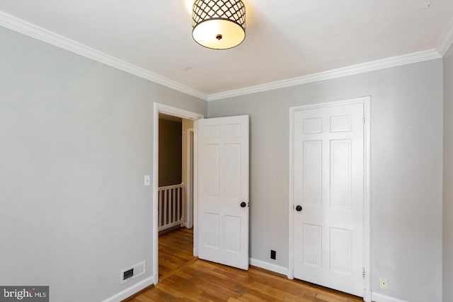unfurnished bedroom featuring visible vents, baseboards, ornamental molding, radiator heating unit, and wood finished floors