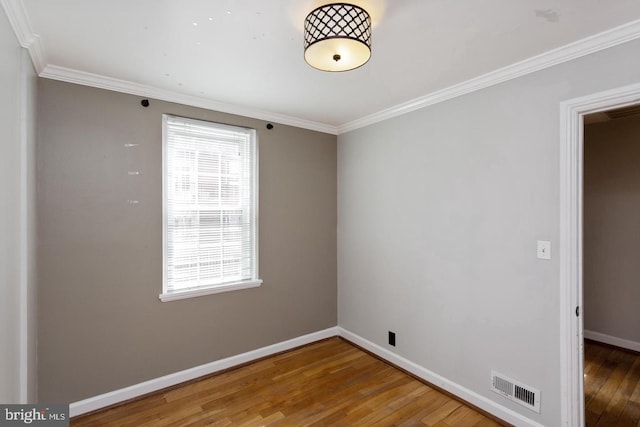 empty room featuring baseboards, visible vents, wood finished floors, and ornamental molding
