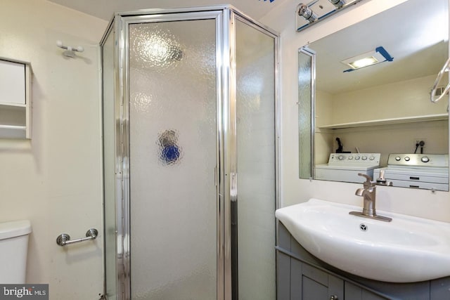 bathroom featuring toilet, washing machine and dryer, vanity, and a stall shower