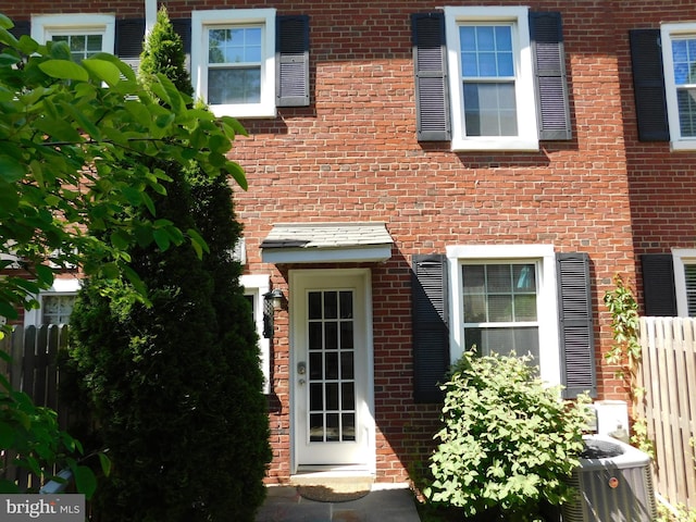 entrance to property with fence, central air condition unit, and brick siding
