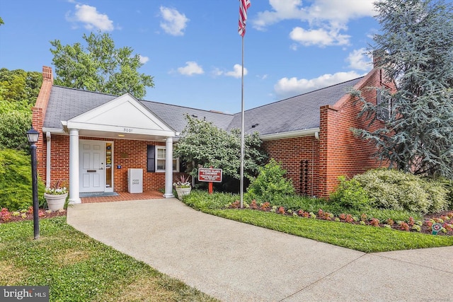 view of front of house featuring a porch, a shingled roof, a chimney, brick siding, and concrete driveway
