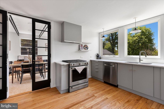 kitchen featuring gray cabinetry, stainless steel appliances, wall chimney exhaust hood, and a healthy amount of sunlight
