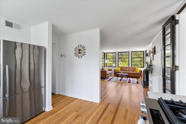 interior space with freestanding refrigerator, light wood finished floors, open floor plan, and visible vents