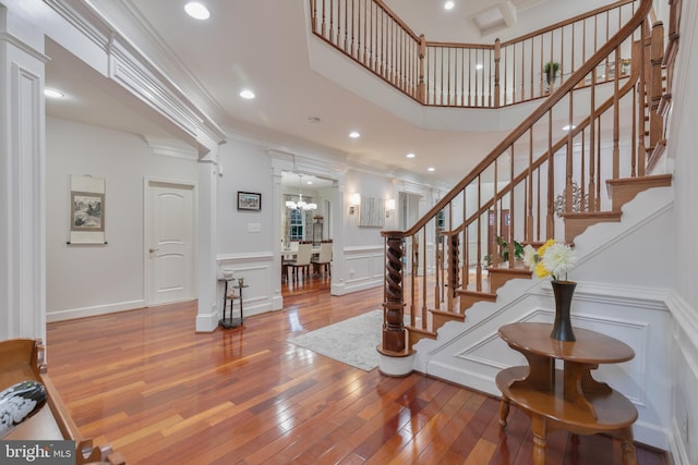stairs featuring a decorative wall, ornate columns, ornamental molding, wood-type flooring, and a notable chandelier