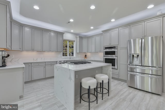 kitchen with light stone counters, a center island, gray cabinetry, stainless steel appliances, and a sink