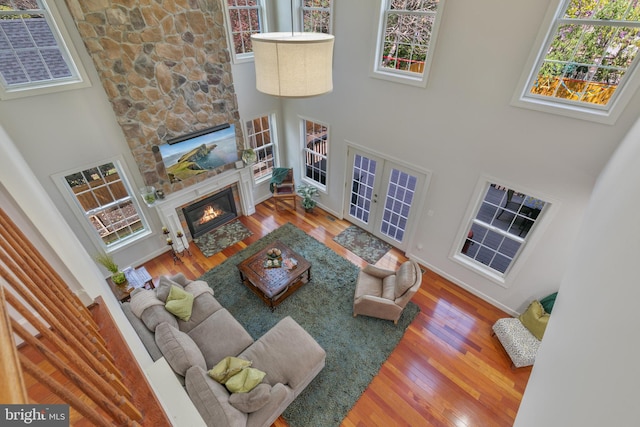 living room with a stone fireplace, wood finished floors, a wealth of natural light, and a towering ceiling