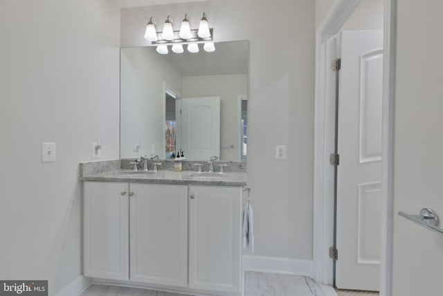 full bathroom with double vanity, marble finish floor, a sink, and baseboards