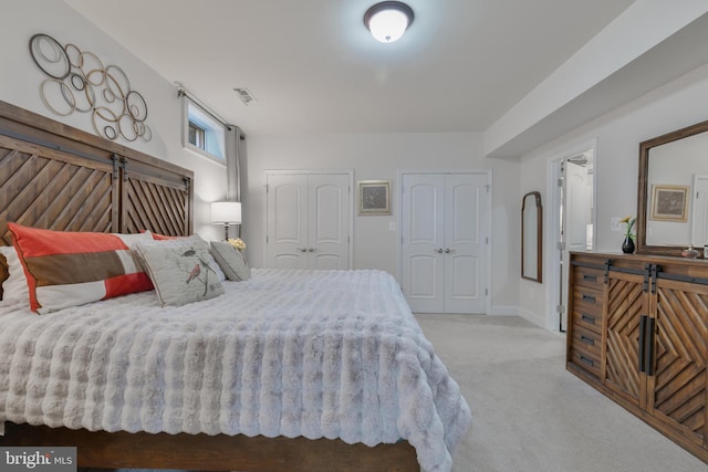 carpeted bedroom with visible vents, baseboards, a barn door, and multiple closets
