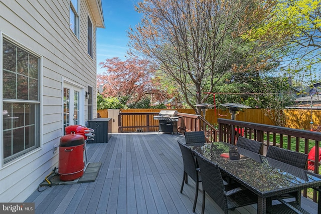 wooden terrace featuring french doors, grilling area, outdoor dining area, and fence