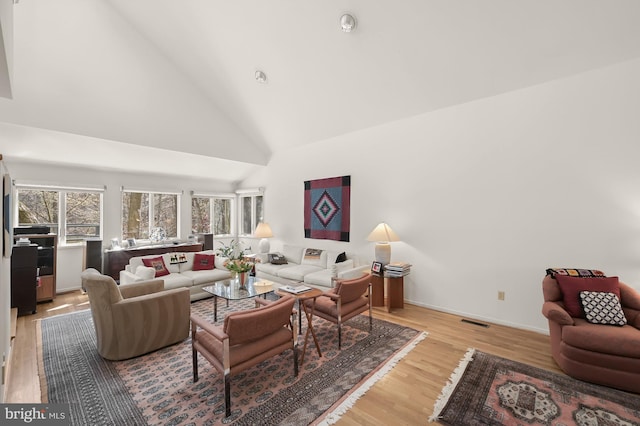 living room featuring baseboards, visible vents, high vaulted ceiling, and light wood-style floors
